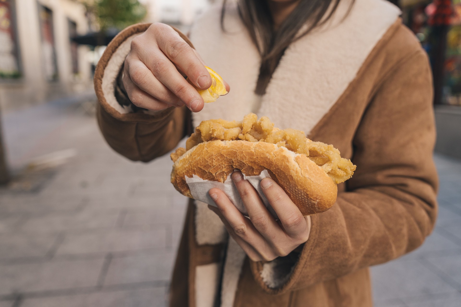 Woman squeezing lemon on fried calamari sandwich in the street Woman squeezing lemon on fried calamari sandwich in the street